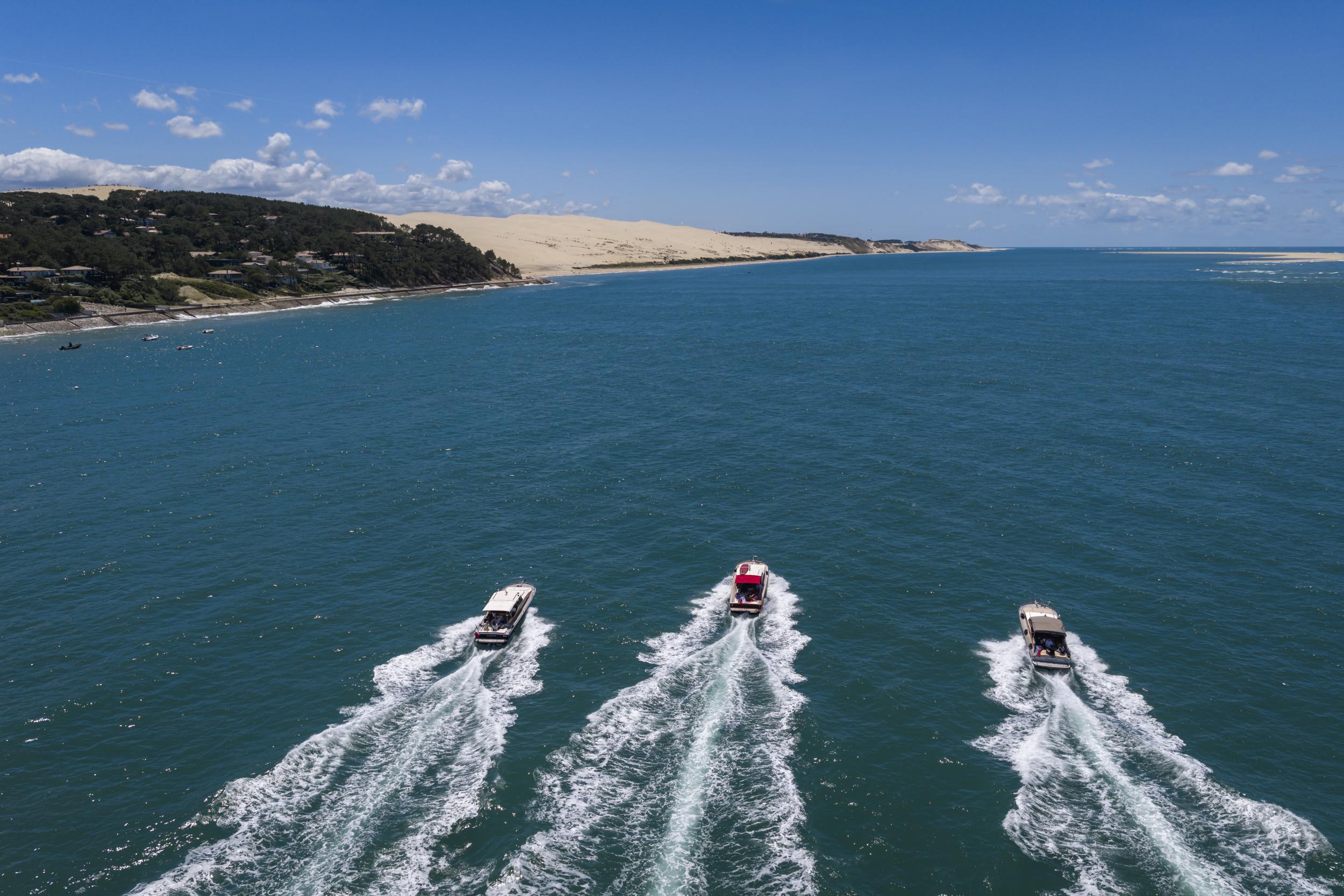 Trois pinasses naviguant de front vers la Dune du Pilat, vues du ciel.